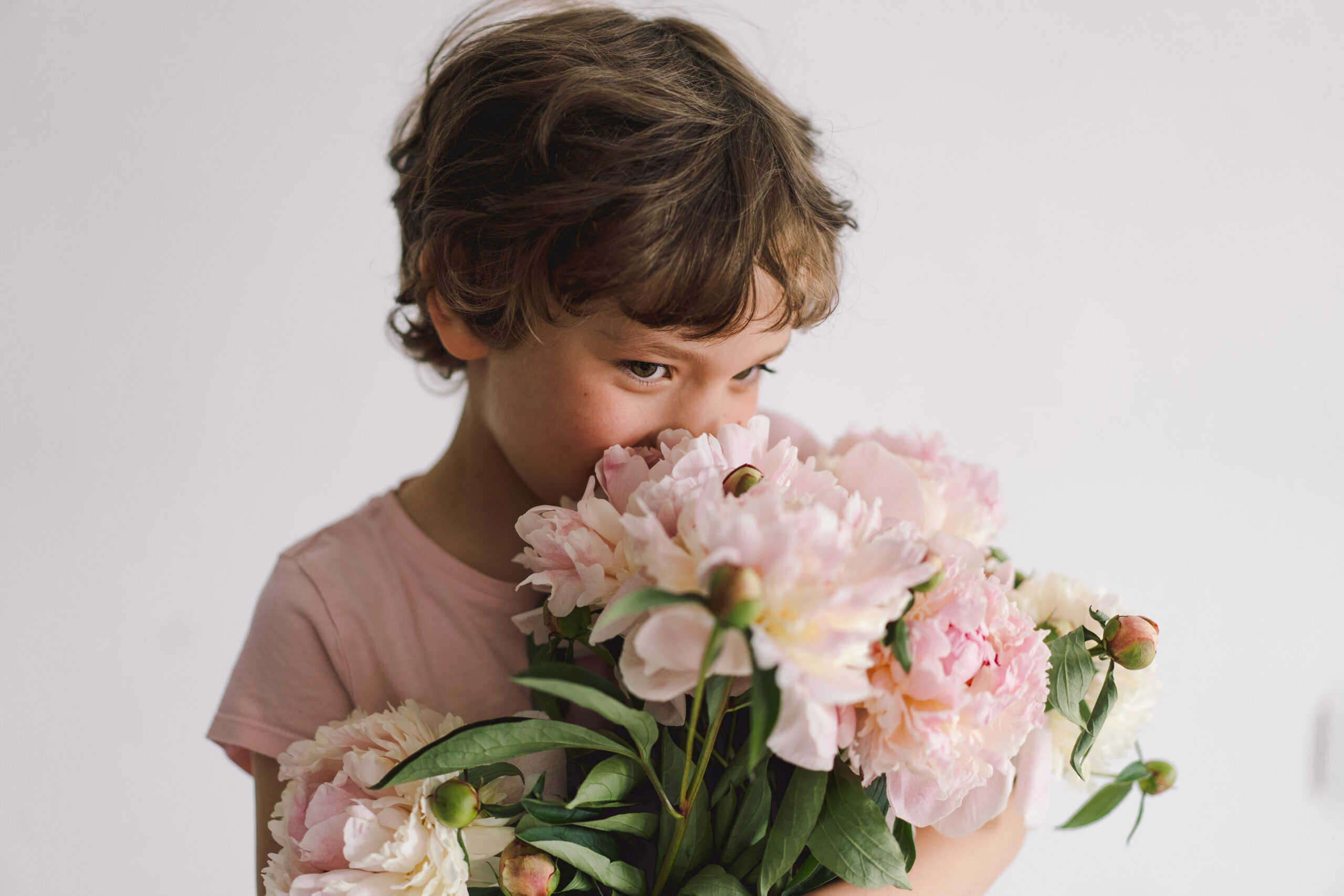 Cheerful happy child with Peonys bouquet. Smiling little boy on white background. Mother's Day. Love and romantic concept